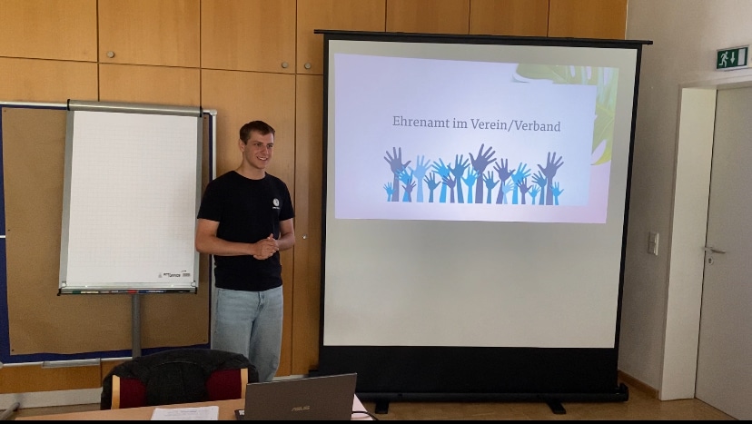 Bundesfreiwilligendienstler Cedric vor der Leinwand bei einem Vortrag. 28. Juli 2024.